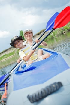 Happy young boy with mother paddling kayak on the river in lovely summer day