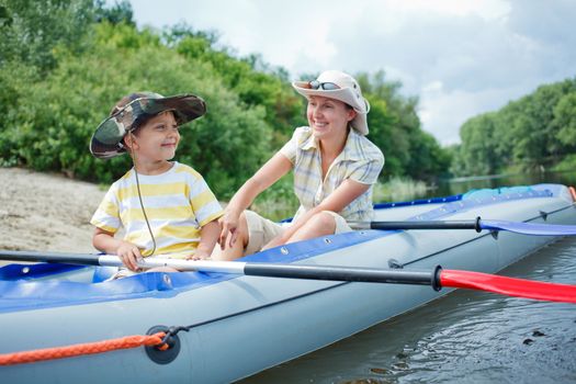 Happy young boy with mother paddling kayak on the river in lovely summer day