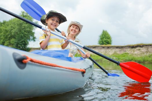 Happy young boy with mother paddling kayak on the river in lovely summer day