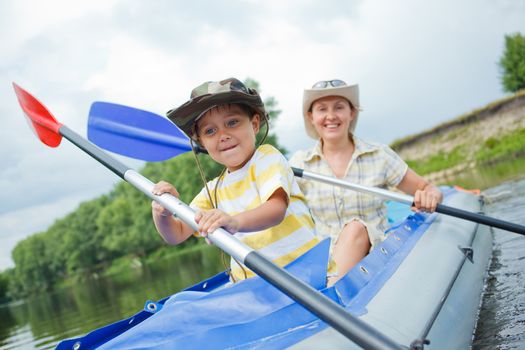 Happy young boy with mother paddling kayak on the river in lovely summer day