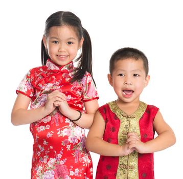 Little oriental girl and boy wishing you a happy Chinese New Year, with traditional Cheongsam standing isolated on white background.