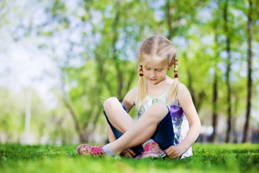 Image of little cute girl sitting on grass in park