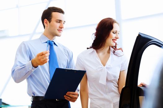 Attractive woman at car salon with consultant choosing a car