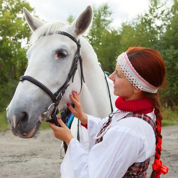 The  girl in traditional Russian costume stroking horse