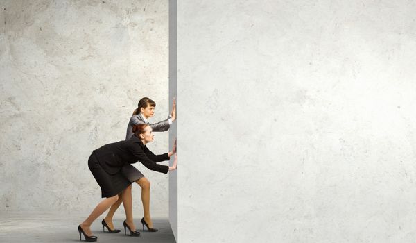 Two businesswoman pushing blank wall. Place for text