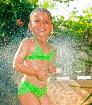Little girl palying with lawn sprinkler in a summer garden