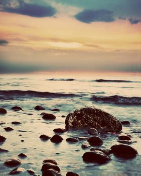 Dramatic sunrise on a rocky beach. Retro, vintage style