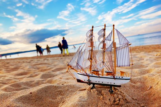 Ship model on summer sunny beach at sunset, ocean in the background. Travel, voyage, vacation concepts 