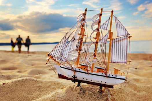 Ship model on summer sunny beach at sunset, ocean in the background. Travel, voyage, vacation concepts 