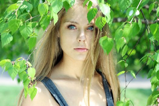 Portrait of the young beautiful woman on a background of leaves of a birch