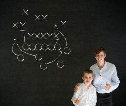 Thumbs up boy dressed up as business man with teacher man and chalk American football strategy on blackboard background
