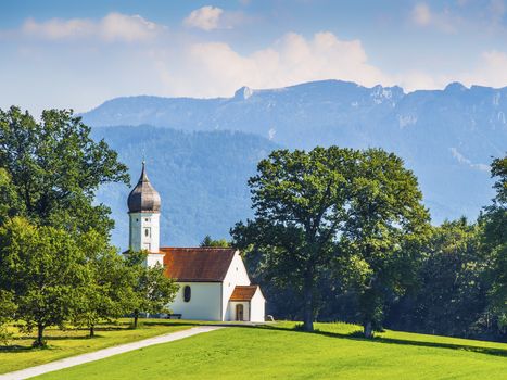 Typical chapel on grean meadow with trees and mountains in Bavarian alps