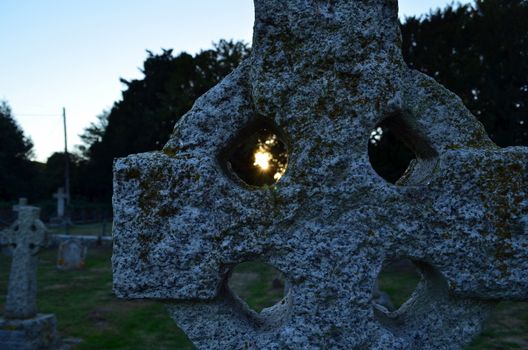 Old English cemetery showing close up of stone Celtic cross with Sun shining through.