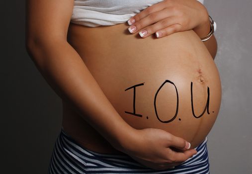 Close-up of the belly of an 8-month-pregnant woman with I.O.U. written on it.