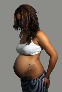 A beautiful young multiracial woman, eight months pregnant, with a tattoo on her belly.