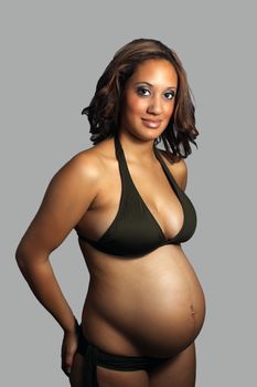 A beautiful young multiracial woman, wearing a bikini, eight months pregnant.