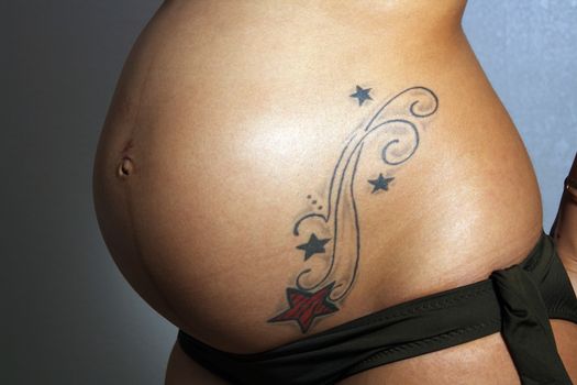 Close-up of the belly of an 8-month-pregnant woman with a tattoo.