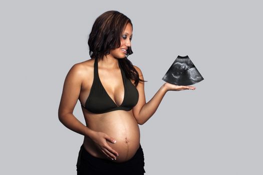 A lovely young pregnant woman holds the ultrasound image of her baby in her hand.