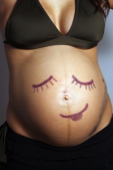 A child-like smiley face drawing on the belly of an eight-month pregnant woman.