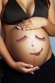 A child-like smiley face drawing on the belly of an eight-month pregnant woman.