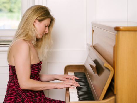 Photo of a happy blond female in her early thirties playing the piano at home.
