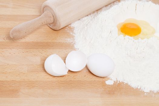 yolk in flour with a rolling pin from top with broken eggs on wooden background