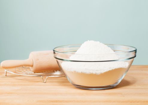 flour in a glass bowl with a rolling pin on with in front of a soft green wall