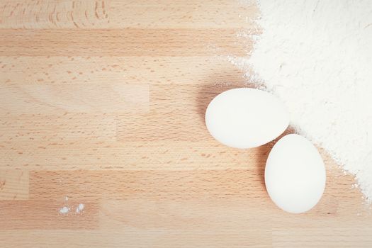 white eggs near flour from top on wooden background with copy space
