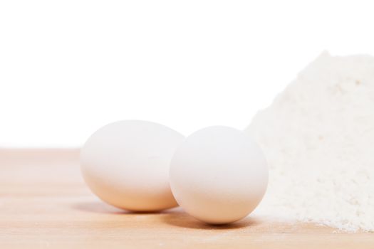 closeup of white eggs near flour on a wooden underground with white background