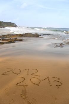 2012 and 2013 written in sand on beach with sea waves starting to erase the word 