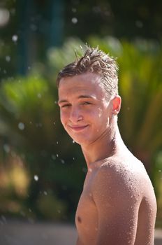 Wet teen in the spray of a fountain in a water park .