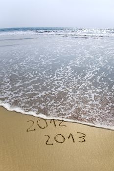 2012 and 2013 written in sand on beach with sea waves starting to erase the word 