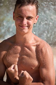 Wet young atletic man showing biceps