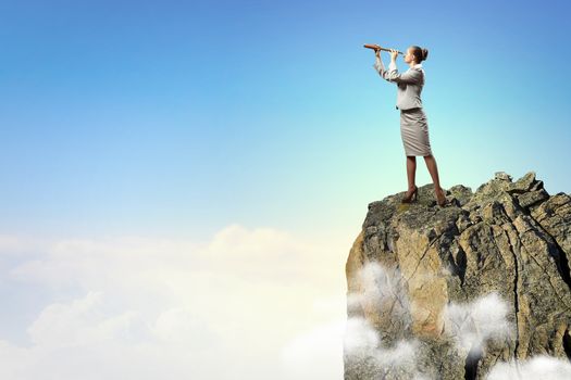 Image of businesswoman looking in telescope standing atop of rock