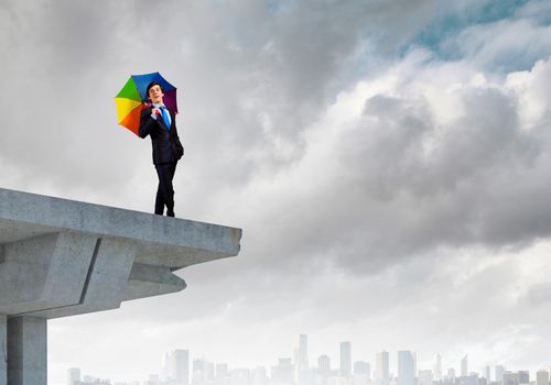 Image of businessman with umbrella standing at the edge of bridge