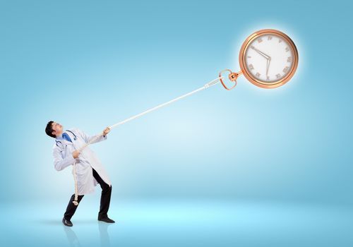 Image of handsome doctor pulling clock with rope