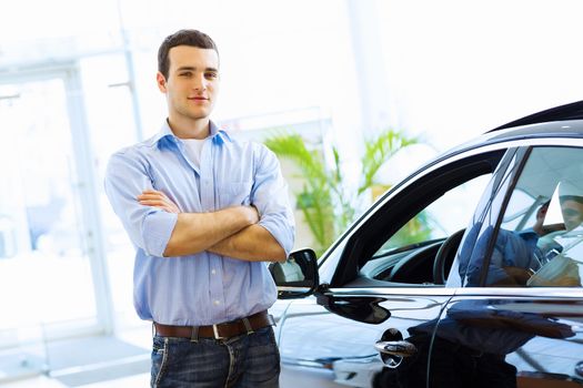 Handsome young man consultant at car salon standing near car