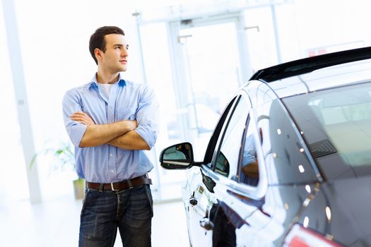 Handsome young man consultant at car salon standing near car