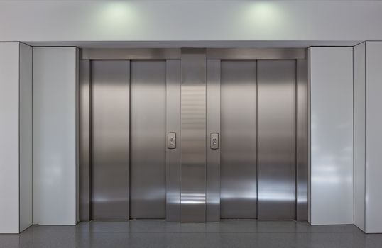 Two brushed metal elevator doors in a minimalistic style building interior 