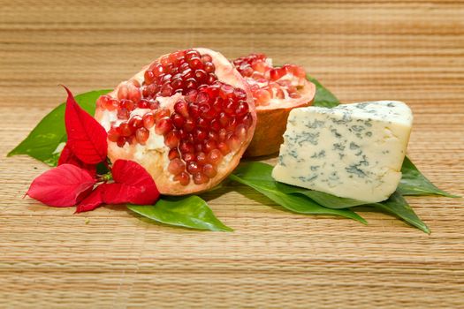 cheese with mold, pomegranate and leaf on matting