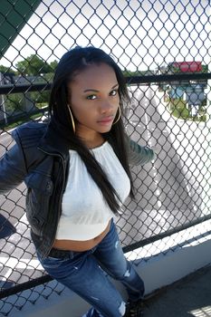 A lovely young Haitian girl on a pedestrian overpass covered with chain-link fence, with the street visible below.