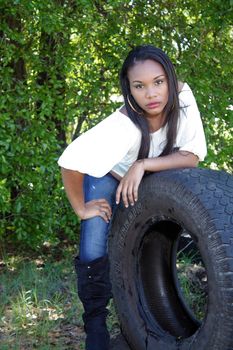 A lovely young Haitian girl leans on a used all-terrain tire outdoors.