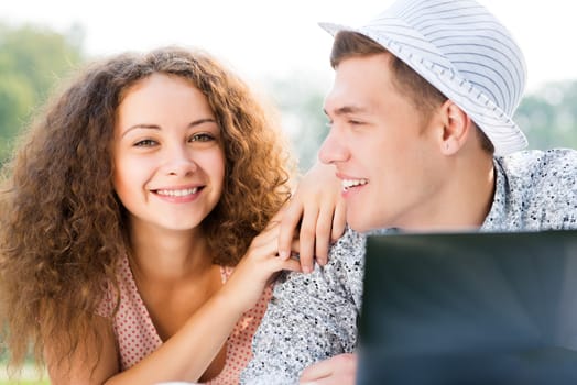 couple lying together in a park, working together on a laptop