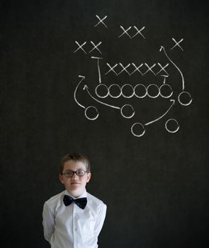 Thinking boy dressed up as business man with chalk American football strategy on blackboard background