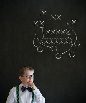 Thinking boy dressed up as business man with chalk American football strategy on blackboard background