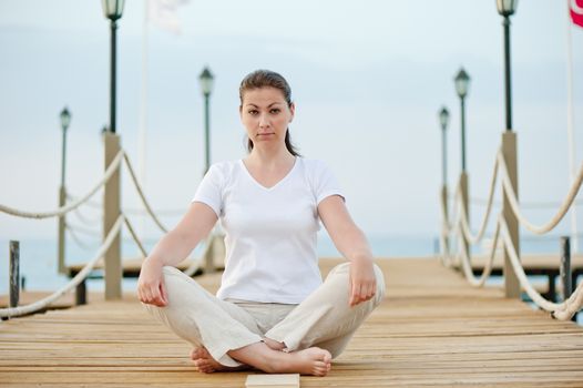 beautiful girl in lotus position resting on the pier at the sea