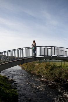 woman silhouetted strolling on a modern bridge over a flowing river