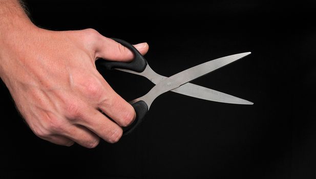An Hand Holding Scissors over a Black Background