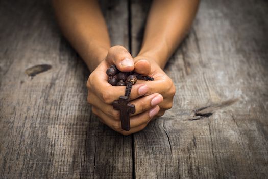 A person praying holding a rosary in the hands on wood background. 