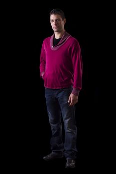 View of a young urban styled fashioned man standing isolated on a black background.